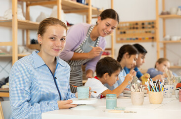 Fototapeta premium Teenage girl paints a ceramic glass made for a master class with a brush. Children make pottery at a workshop in a creative studio