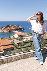 Adult woman wearing casual clothes standing on viewpoint terrace with sea and island in background, summer vacation lifestyle, travel and tourism concept, outdoor leisure, copy space
