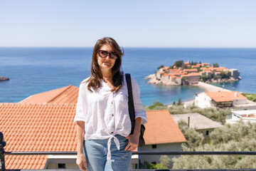 Adult woman wearing casual clothes standing on viewpoint terrace with sea and island in background, summer vacation lifestyle, travel and tourism concept, outdoor leisure, copy space
