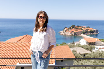 Adult woman wearing casual clothes standing on viewpoint terrace with sea and island in background, summer vacation lifestyle, travel and tourism concept, outdoor leisure, copy space