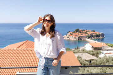 Adult woman wearing casual clothes standing on viewpoint terrace with sea and island in background, summer vacation lifestyle, travel and tourism concept, outdoor leisure, copy space