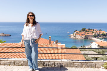 Adult woman wearing casual clothes standing on viewpoint terrace with sea and island in background, summer vacation lifestyle, travel and tourism concept, outdoor leisure, copy space