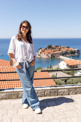 Adult woman wearing casual clothes standing on viewpoint terrace with sea and island in background, summer vacation lifestyle, travel and tourism concept, outdoor leisure, copy space