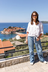 Adult woman wearing casual clothes standing on viewpoint terrace with sea and island in background, summer vacation lifestyle, travel and tourism concept, outdoor leisure, copy space