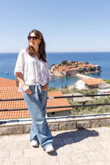 Adult woman wearing casual clothes standing on viewpoint terrace with sea and island in background, summer vacation lifestyle, travel and tourism concept, outdoor leisure, copy space