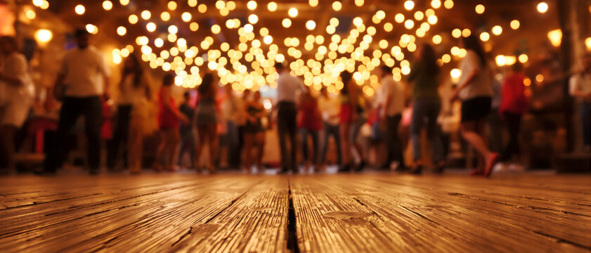 Blurred night party background featuring crowd of people dancing under warm string lights with sharp textured wooden floor perspective for montage, product display or celebrating event concepts
