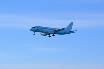 Obraz premium White aircraft on final approach to the airfield under a bright blue sky.