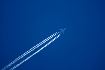 Jet airliner leaving long contrail in deep blue sky, close-up. Passenger airplane with distinct vapor trail against clear blue sky