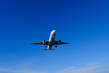White commercial airplane approaching against clear blue summer sky. Commercial airliner coming in for landing, blue summer sky background