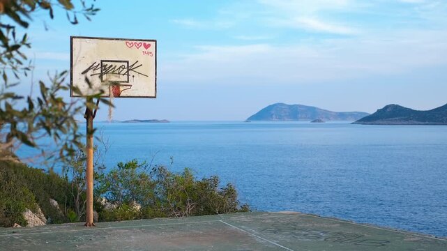 Abandoned basketball court overlooking the serene ocean. Picturesque coastal scenery featuring an old, weathered basketball court with a graffiti-covered backboard on a cliff edge, overlooking the sea