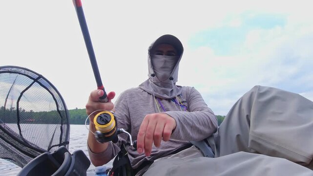 Kayak sport fishing. Angler enjoys kayak fishing at scenic coastline, casting his rod and reeling. Peaceful water shore and perfect setting at lake Simcoe, Ontario, Canada. Catch and release panfish.