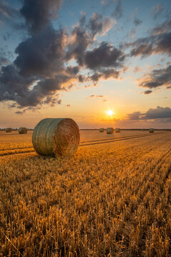 Strohballen auf einem Feld im goldenen Sonnenuntergand und atemberaubender Wolkenstimmung
