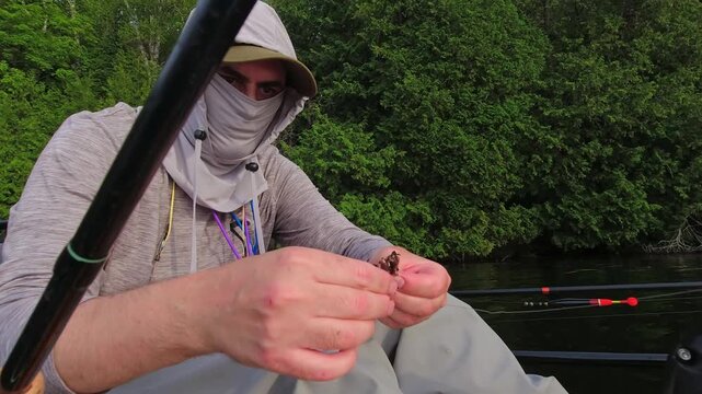 Angler put night crawler bait on fishing hook, drop shot fishing technique. Kayak sport fishing. Angler enjoys kayak fishing at scenic coastline. Peaceful water setting at lake Simcoe, Ontario, Canada