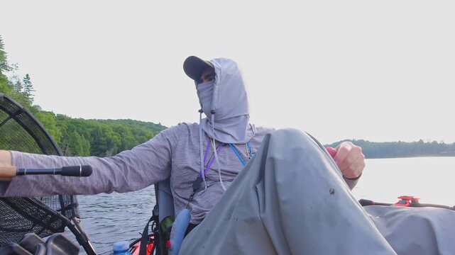 Kayak fishing solitude at lake Simcoe in Ontario, Canada, surrounded by stunning nature and tranquility. Angler enjoys solitude during hot summer evening. Man casts and reels his spinning rod.