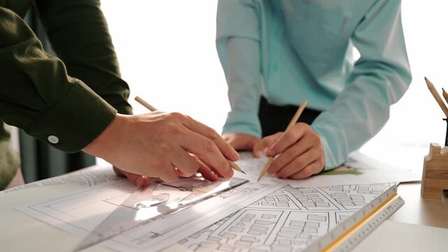 Smart architect and safety engineer discussion about building blueprint on table with architectural document, measurement tools and wooden block scatter around at modern office. Closeup. Delineation.