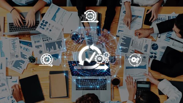 A team of professionals collaborates in an office setting, analyzing data and charts to drive improvements in efficiency and project success using technology and teamwork. Raster