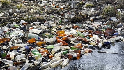 Dirty river is polluted with many plastic bottles. A lot of trash is dumped in open and freely available places at nature. Global environmental pollution problem. Concept of ecological disaster