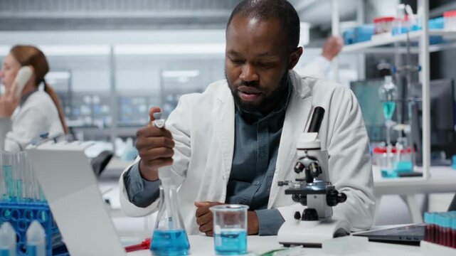 Assay development specialist pipetting reactant into blue solution for purity analysis. Man in research facility lab adding liquid agent to test tube to observe chemical reaction properties, camera B