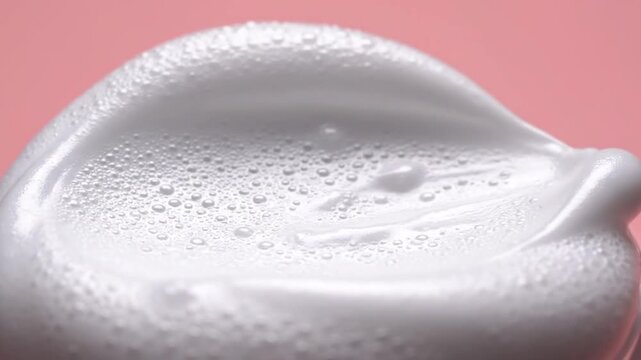 Close-up of fluffy white foam with small bubbles and smooth textures on a pink background for skincare or cosmetic advertising