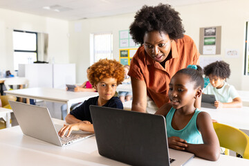 African American teacher wearing orange helping youth female in teal top using laptop in classroom