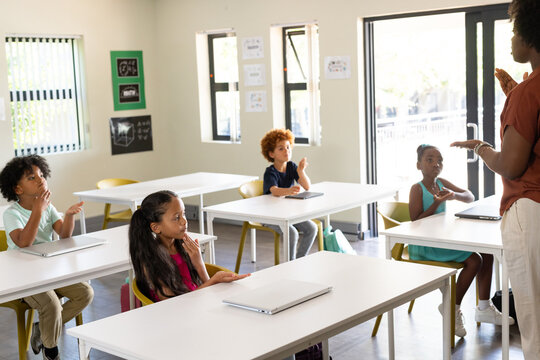 African American teacher with four youth students teaching in class with desks and closed laptops