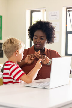 African American teacher in rust shirt at school showing finger counting, youth pointing at laptop