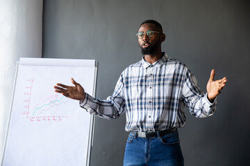 African American mid-adult male speaking and gesturing at meeting flipchart, wearing plaid shirt