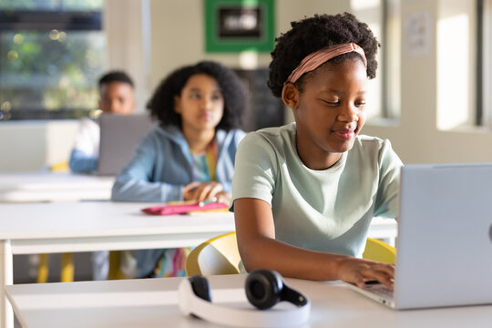 African American teenage students working on silver laptop and headset in class, copy space