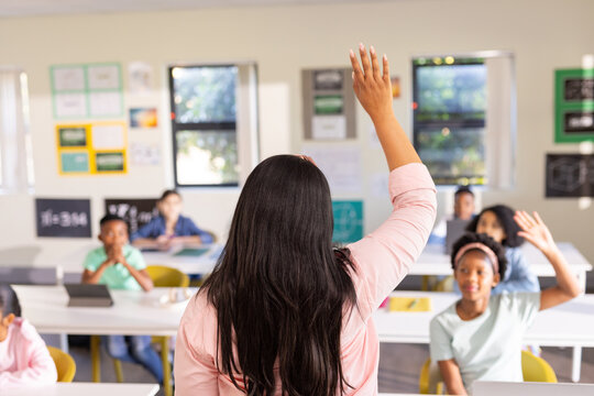 African American female teacher standing at front of class, raising hand, students sitting at desks