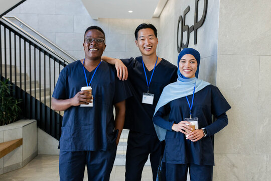Diverse medical staff wearing navy scrubs standing in hospital lobby holding cups and blue IDs