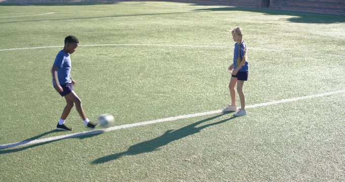 Diverse youth teammates practicing ball control, boy flicking soccer ball to girl on turf sideline