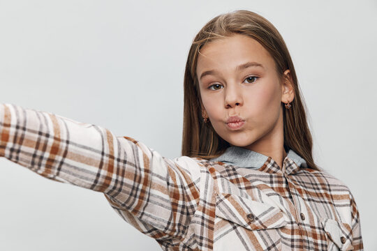 Teenage girl with long hair wearing plaid shirt making a selfie with pout lips on white background. Casual style, youth and social media concept.