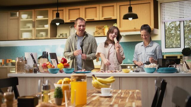 Family with tween girl singing and dancing around in the kitchen, acting silly and laughing together for fun weekend activity. Goofy daughter and parents using utensils for karaoke. Camera A.