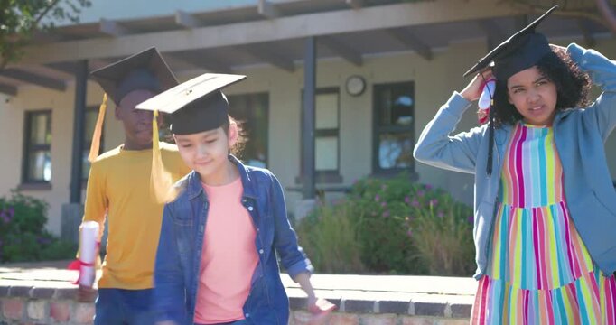 Diverse children at graduation cue stepping forward on school wall waving diplomas with tassels