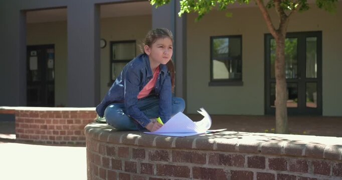 Female preteen finding courtyard spot sitting on brick wall and marking sheets with yellow marker