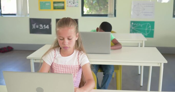 Diverse children in class typing on laptops while camera tightening drawing girl pausing, thinking