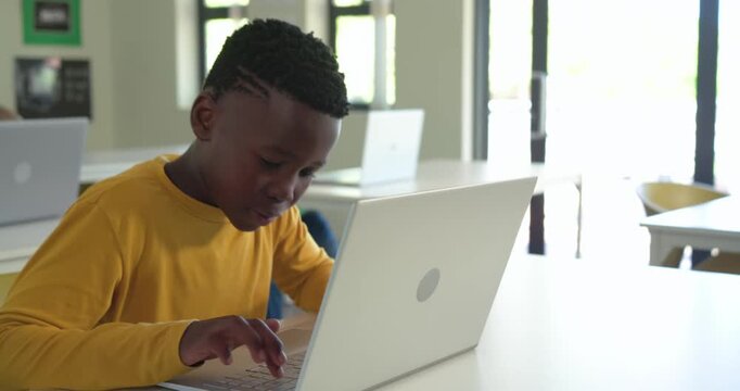 Classmates, African American boy wearing yellow shirt typing on laptop for classwork in classroom