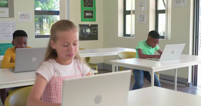 Diverse child classmates watching green-shirt boy finishing laptop, walking to front desk, sharing