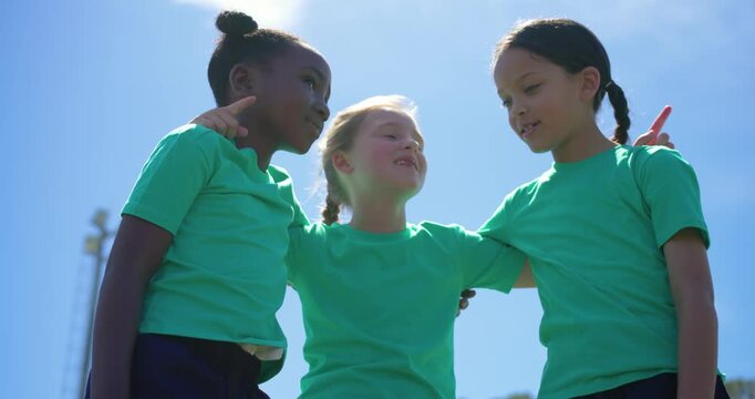 Three female children pre-game huddling stacking palms and raising arms on field wearing green tees