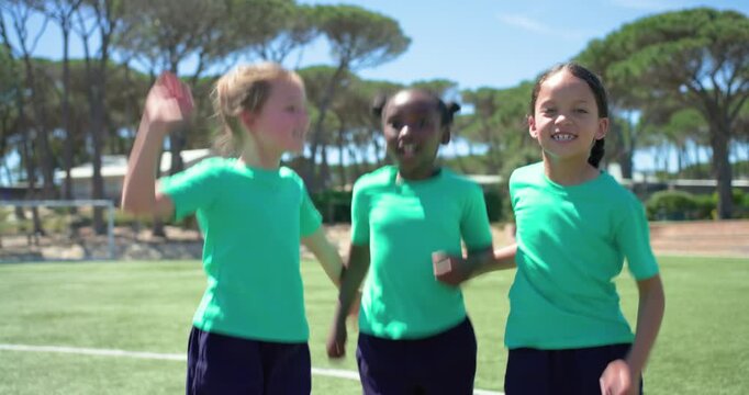 Diverse female children after posing, starting jumping in sync on sports field wearing green tees