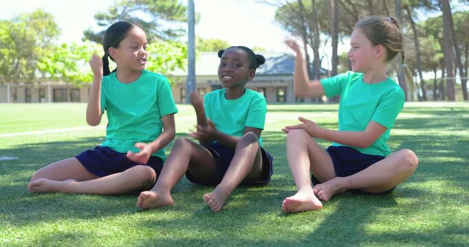Diverse female children following clap cue, playing clapping game on turf taking turns in green