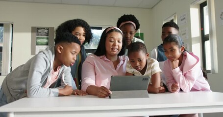African American teacher in pink opening tablet in class teaching kids as one tapping screen - Powered by Adobe