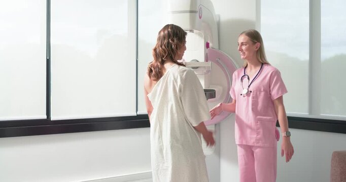 Female patient entering gowned and female scrub tech preparing mammogram adjusting paddle at clinic