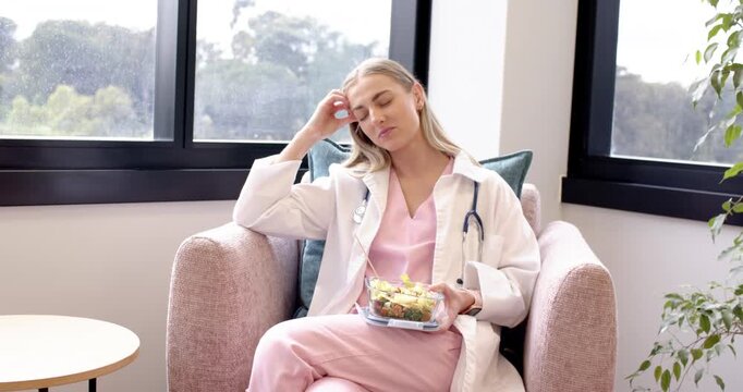 Adult female in scrubs with stethoscope taking break in staff lounge picking fork eating salad