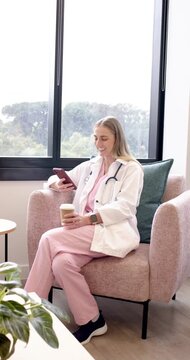 Vertical video: Female MD after sipping coffee reading text, scrolling smiling in lounge with steth