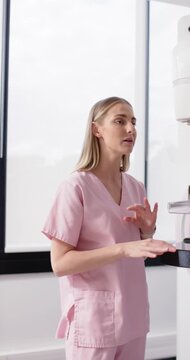 Vertical video: Adult female in pink scrubs in clinic starting demo showing machine with hand moves