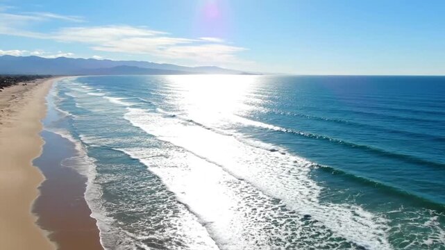 Aerial view of a sunny beach with gentle waves on a beautiful day with mountains in the background