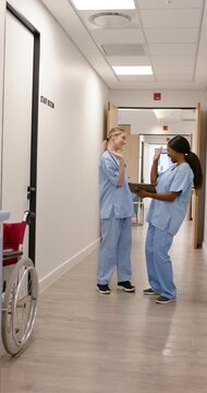 Vertical video: Diverse female RNs in scrubs noting clipboard for rounds, high-fiving walking ward