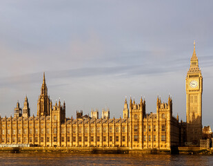 Obraz premium Palace of Westminster and Big Ben illuminated by golden hour light, reflecting on the River Thames in London