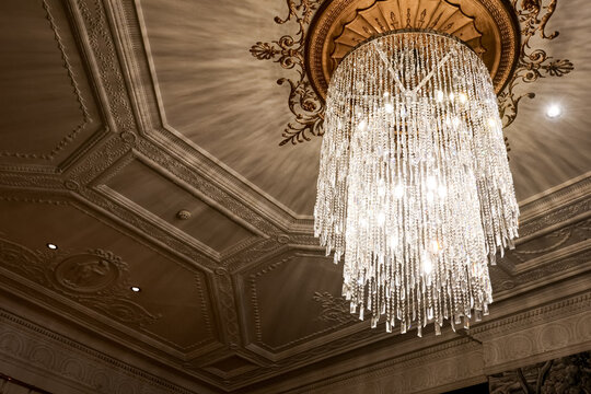 Ornate crystal chandelier illuminating a decorative ceiling with elegant plasterwork, creating a luxurious interior ambiance in London